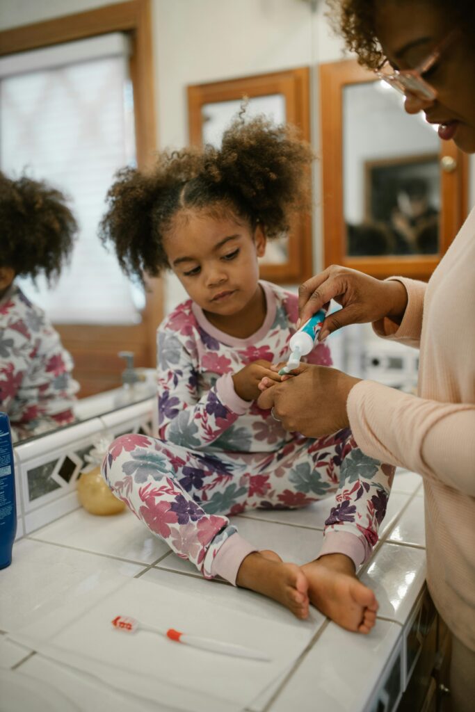 A mother assists her daughter with brushing teeth during a morning routine, fostering hygiene habits.